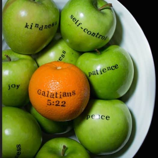 Green apples in a bowl with one orange labeled 'Galatians 5:22', symbolizing the fruits of the Spirit.